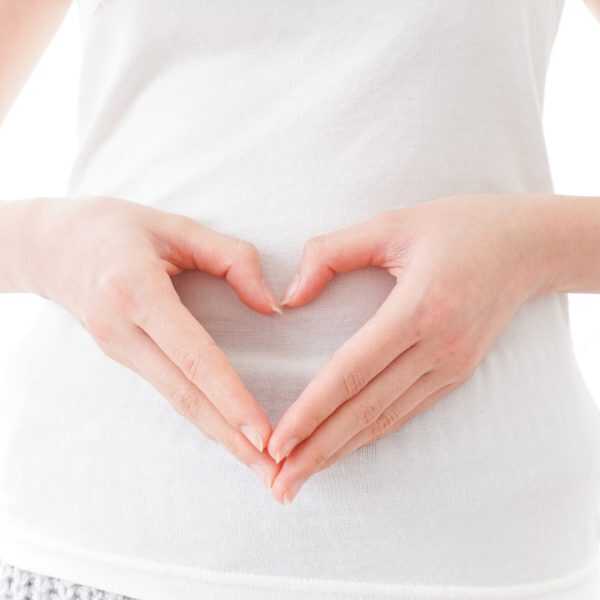 A person's hands forming a heart shape over their white-shirted abdomen, symbolizing gut health.