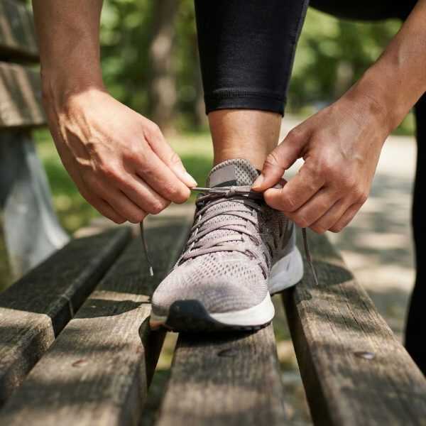 Hands tying running shoe laces in a sunlit park.